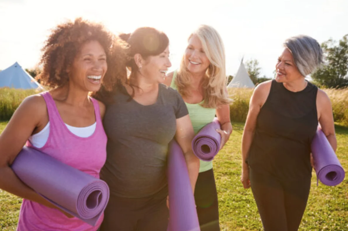 Group Of Mature Female Friends On Outdoor Yoga Retreat Walking Along Path Through Campsite
